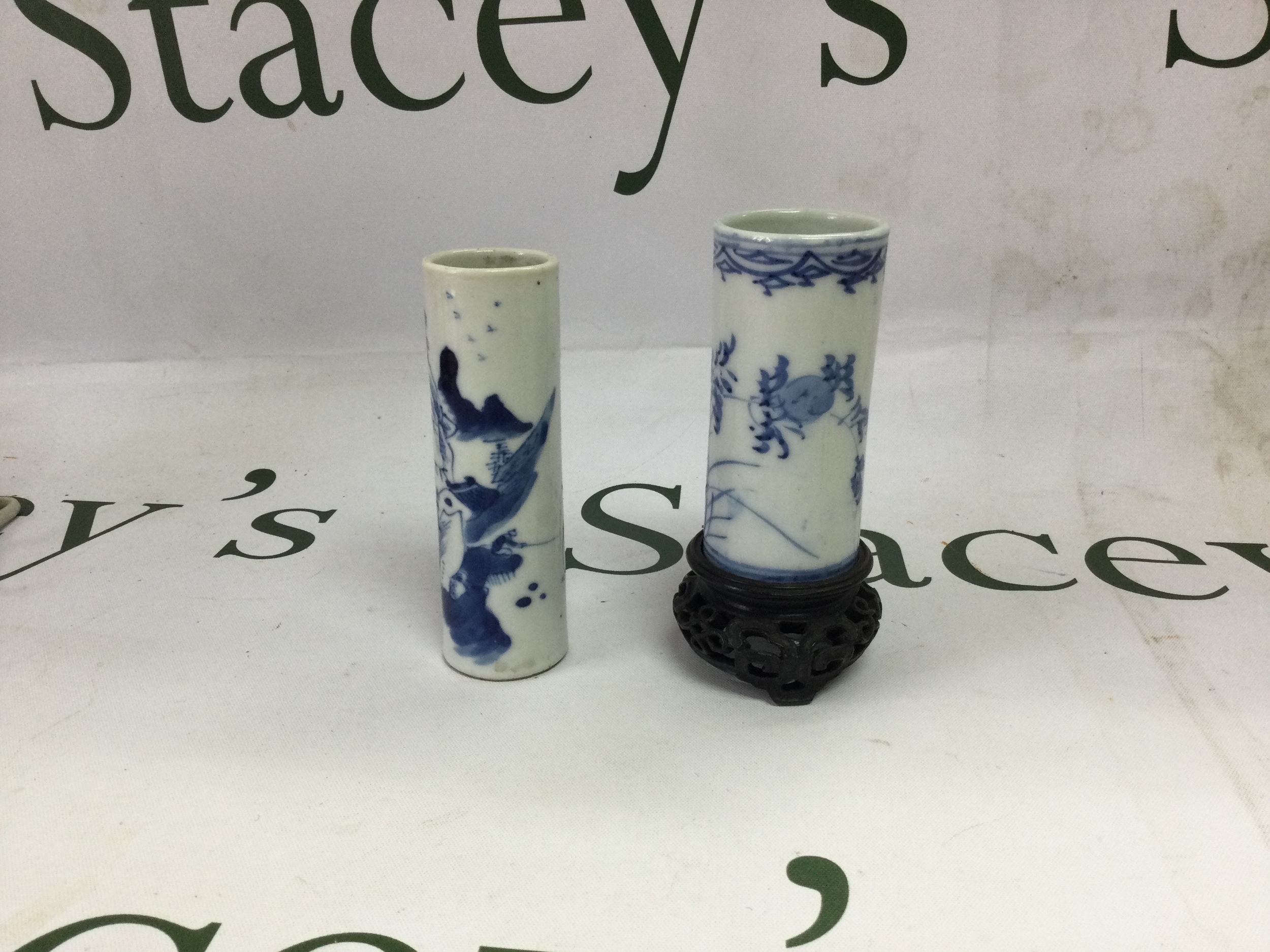 Kang Xi cylinder vase depicting man fishing with a mountainous landscape to foreground, 10 cm x 3cm, and a later example  decorated with foliage on a wooden stand 8 cm x 3.5 cm both free from any damage.