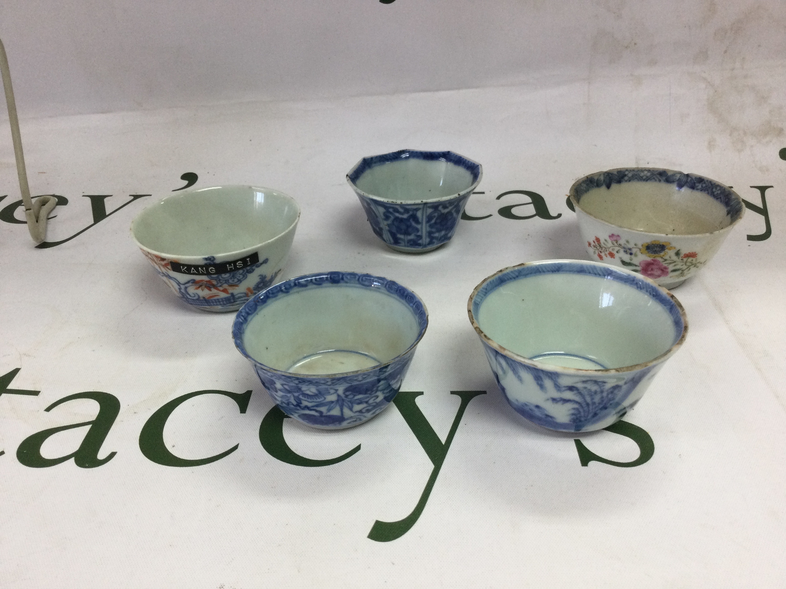 Five 17/18th C Chinese cups,  red and blue pattern example with bridge under prunus tree having a red flower to the inside has minor chips to the rim. the octagonal example with floral cartouches to outer and a Lingzhi mushroom to the inside, minor flitting to the rim and a chip to the base rim. the coloured floral example has a lobed rim with minor chips and blue and white patterned interior. blue and white floral decorated example with banded design rim has minor chips to the rim and floral decoration to the interior. blue and white detracted example of a fisherman under tree, chips and flitting to the rim. all approx 7cm x 3.5 cm -4 cm