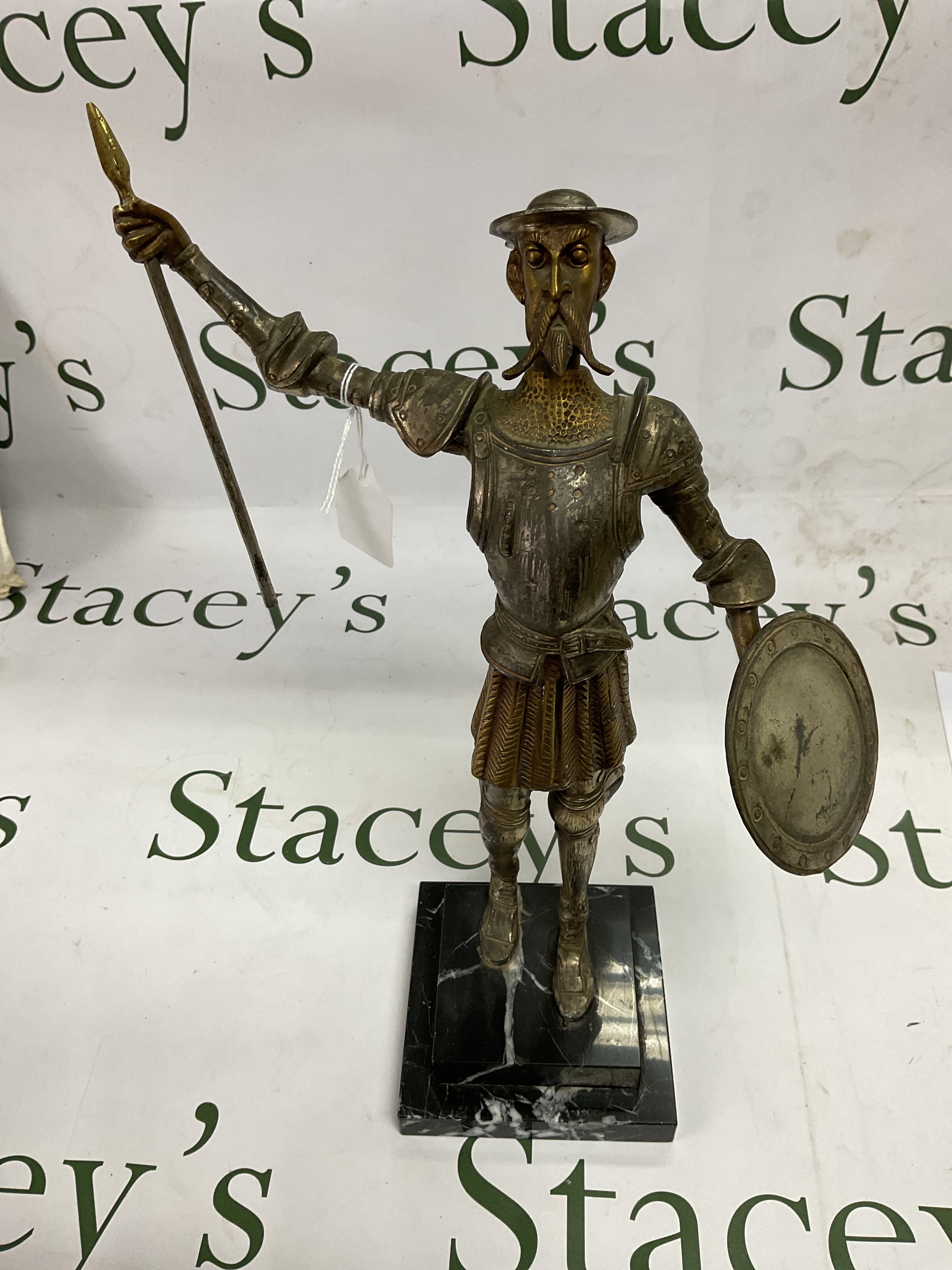 Bronze figure of Don Quixote, on a stepped black marbled base, dressed in his armour with shield and half a spear. 40cm high.