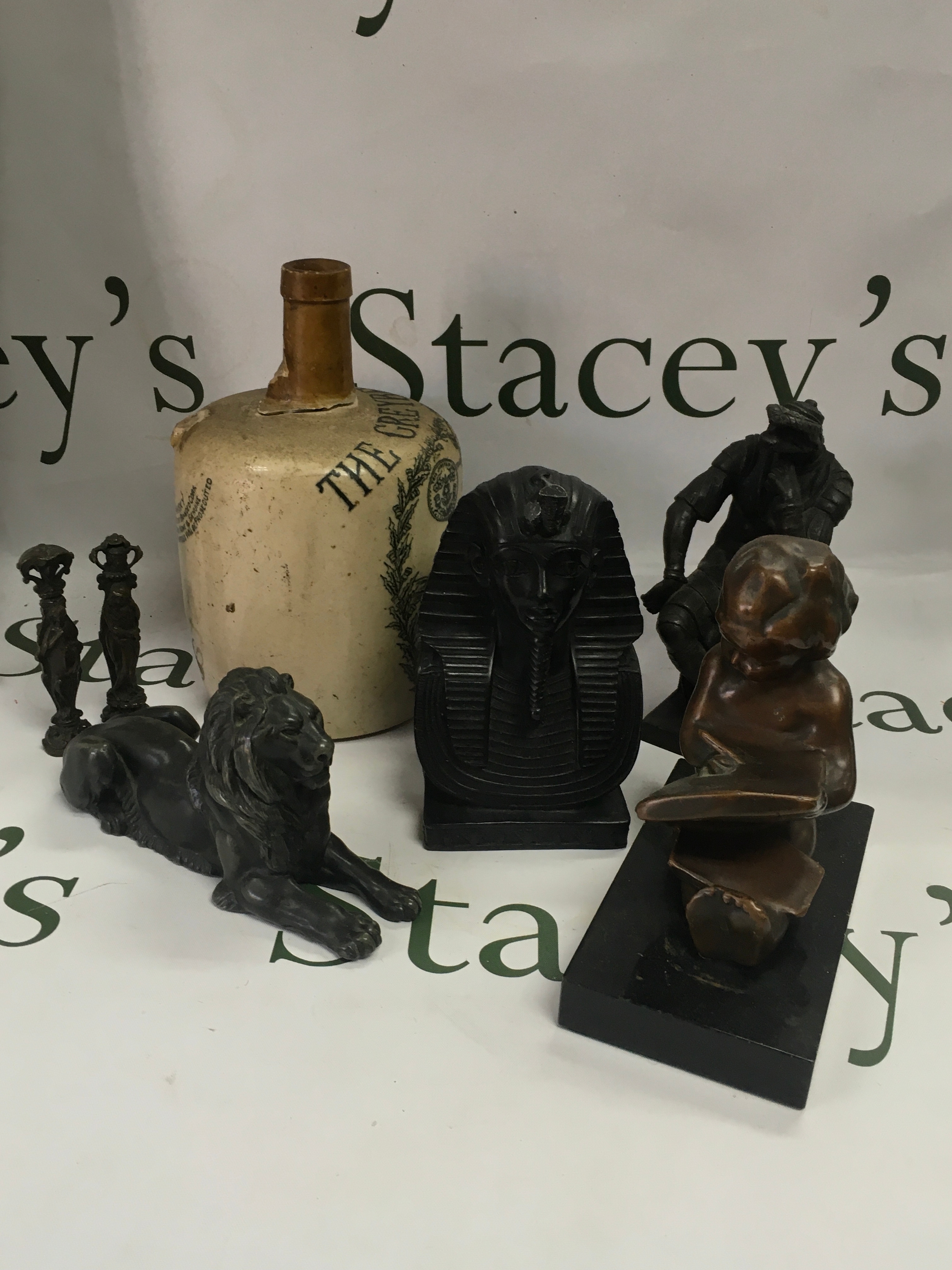 A collection of vintage an antique decorative objects including: a stoneware flagon which is damaged as the top of the flagon has been cracked off, reclining lion figure, Egyptian Pharaoh Bust, Seated Figure Sculpture, two metal desk seals and a sculpture of a child drawing. 