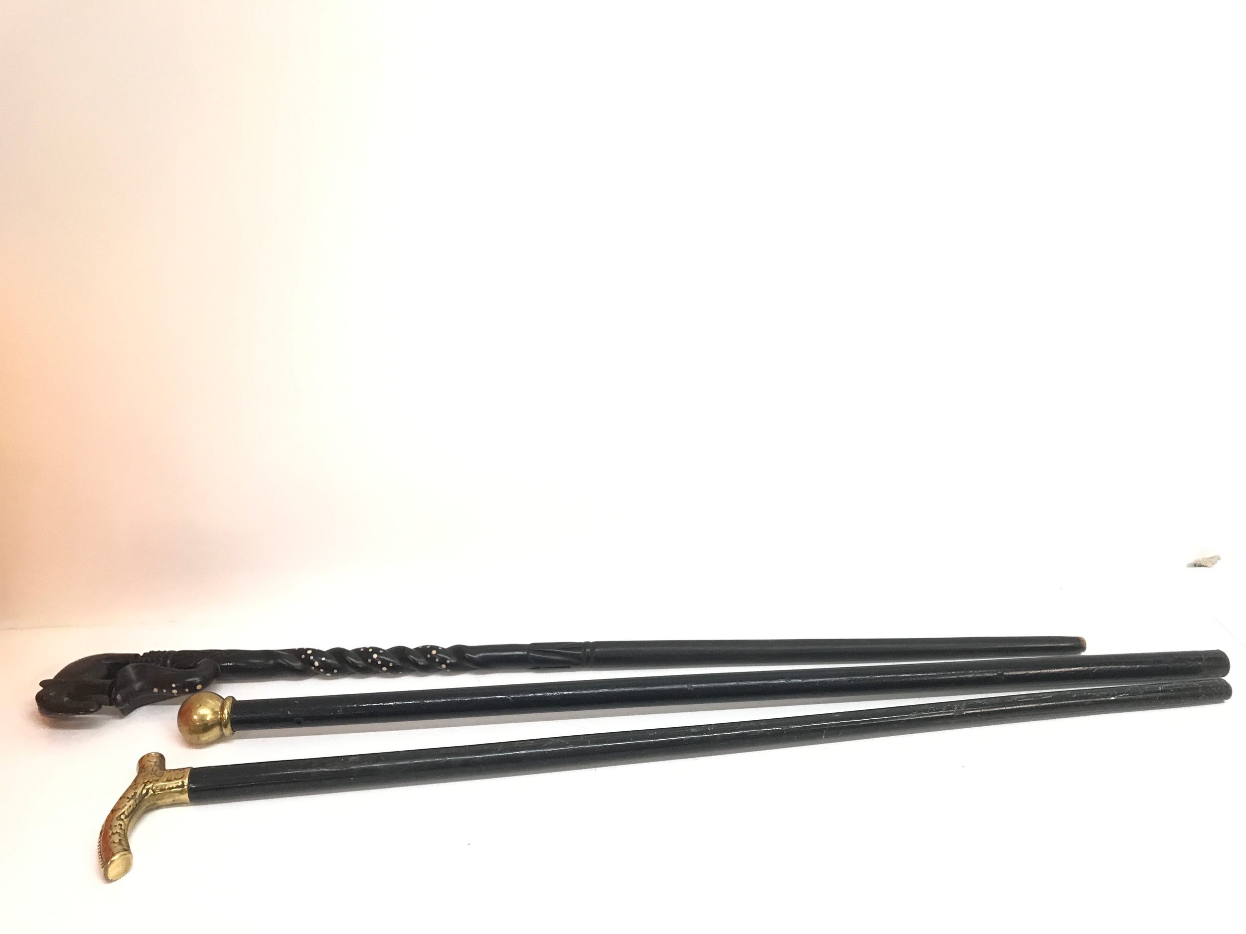 Three walking sticks including two with brass handles and one with an elephant design. Approx 87cm long