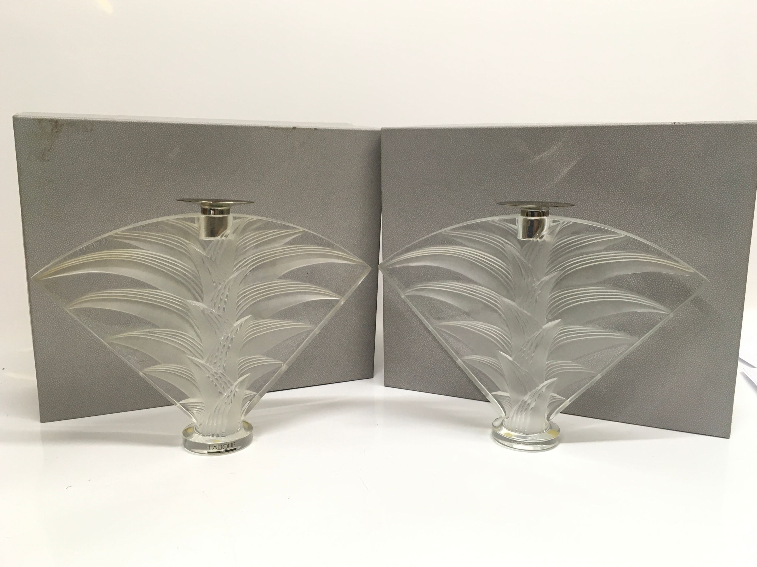 Two boxed Lalique Ravelana crystal candlesticks features a fan-shaped design with clear and frosted glass. 22cm tall 28cm wide