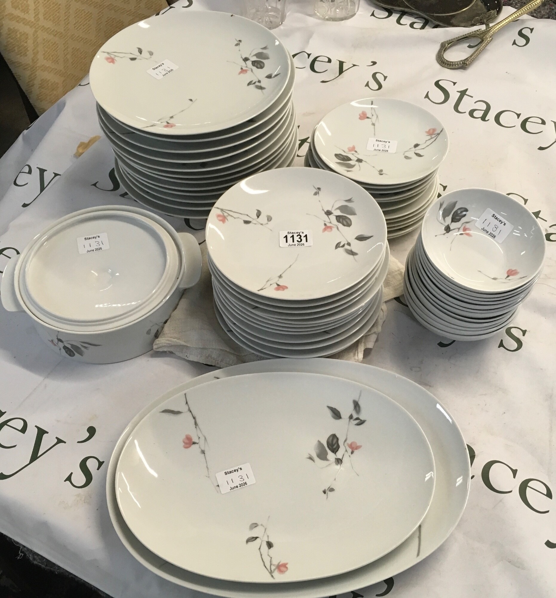 A set of ceramic table equipment. The patterns feature delicate, stylised grey branches and leaves bearing minimalist coral blossoms reaching across a clean white ceramic glaze
