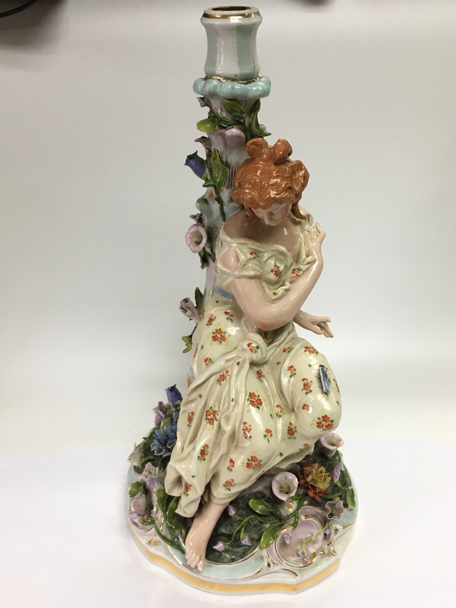 A German figural candlestick in the form of a maiden seated and surrounded by flowers, approx height 36.5cm. Some damage. NO RESERVE