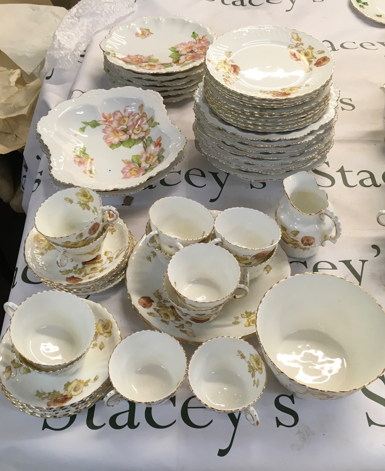 A collection of ceramic table ware consisting of delicate stylised flowers and leaves in warm autumn tones of amber. Also, this set contains dishes that have vibrant hand-coloured pink and yellow wild roses on trailing branches with bright green foliage