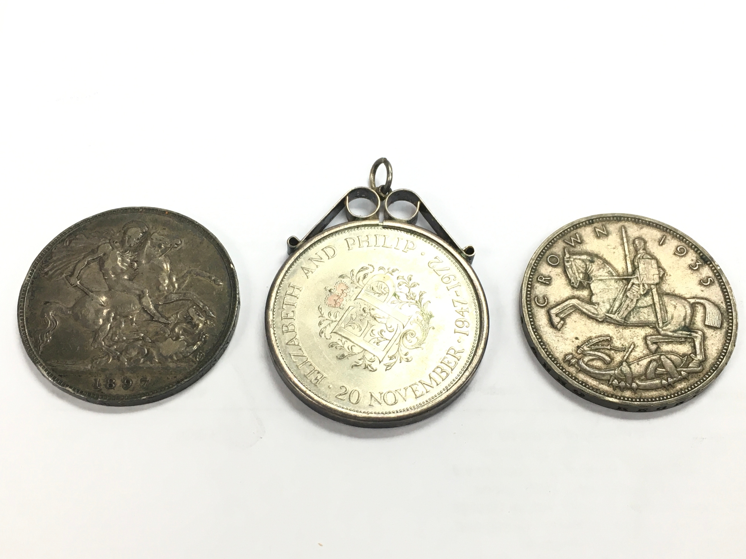 Three coins- Queen Victoria 1897 silver crown, a 1972 Queen Elizabeth and Prince Philip Silver Wedding commemorative coin mounted as a pendant and a King George V 1935 silver wreath crown 