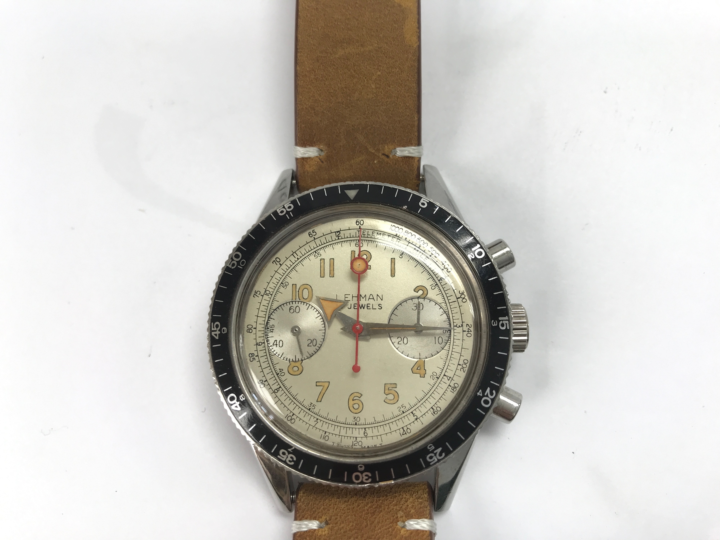 vintage Lehman 17-jewel chronograph wristwatch with a cream dial, Arabic numerals, two subsidiary dials, a red chronograph seconds hand, and a rotating black bezel on a brown leather strap.