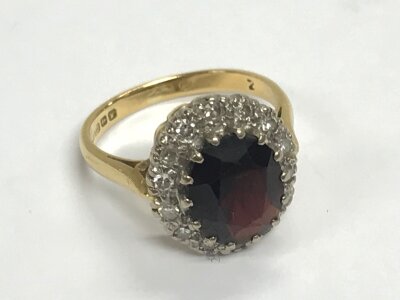 A garnet and diamond ring with 15 (26 cuts) diamond around a garnet measuring 11.5x8.5x4.5mm set in 18ct gold Birmingham 1970. 5.2g total weight. Size K