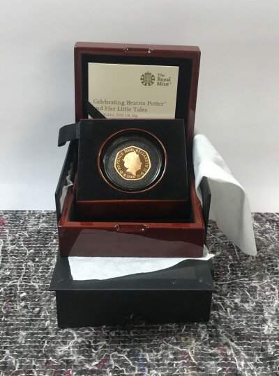Beatrix Potter and Her Little Tales, Peter Rabbit 2020 UK 50p Gold Proof Coin. Alloy- 916.7 Au, Weight- 15.50g. A Royal mint commemorative issue from the 'Celebrating Beatrix Potter and Her Little Tales' series, featuring Peter Rabbit. Presented in its original fitted wooden case with certificate of authenticity and outer packaging. The coin displays a portrait of Peter Rabbit based on the illustrations of Beatrix Potter and was stuck to proof standard for collectors.