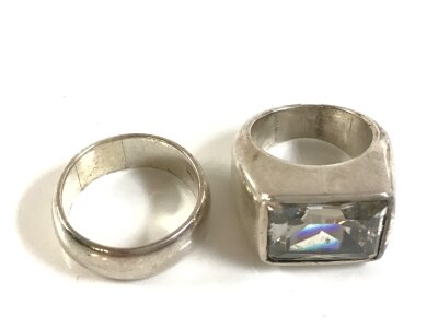Two silver rings, wedding ring style and the other a clear stone