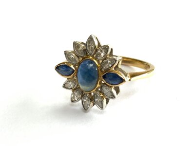An 18ct yellow gold and platinum ring of floral design set with  a central cabochon sapphire,  surrounded by marquise cut diamonds and sapphires in the form of petals. Size R.