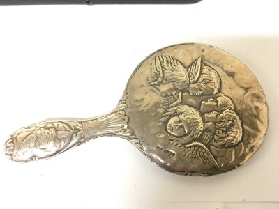 A Silver backed mirror Chester hallmarks decorated with raised cherubs.