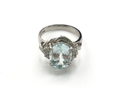 A platinum ring set with an oval aquamarine flanked by RBC diamonds and patterned shoulders. Aquamarine 4.33ct and 0.10ct diamonds. Size 
Size L
