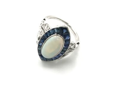 Platinum navette ring set with an oval cabochon Opal surrounded by calibre cut sapphires and accent diamond set fancy shoulders. Approximately 1.85ct Opal and 2ct sapphires. Size M 1/2