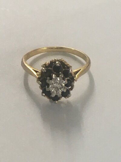 A 18 ct gold ring inset with single diamond surrounded by sapphires .