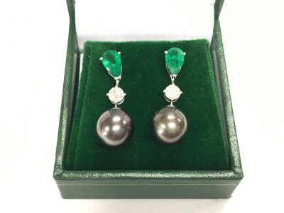 A pair of 18ct white gold fancy drop earrings set with pear shaped emeralds diamonds and suspended dark pearls. Emeralds 1.40ct and diamonds 0.52ct approximately.