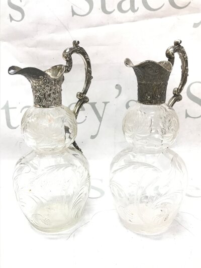A pair of glass claret jugs with silver hallmarked tops. 23cm tall