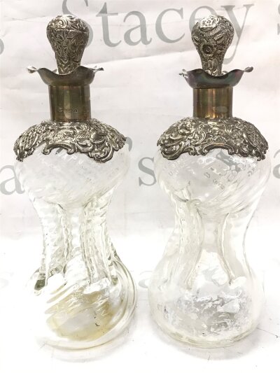 A pair of glass 'glug glug' decanters with silver hallmarked tops, one damaged. 27cm tall