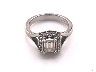 An 18ct white gold ring set with a rectangular diamond flaked by chip diamonds, central diamond approximately 0.70ct. 
Size I 1/2