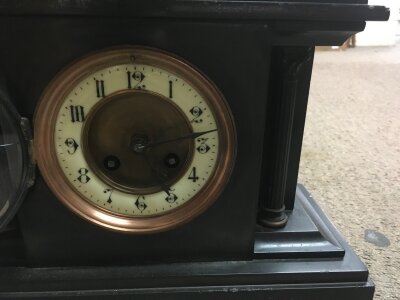 A black slate mantle clock the circle dial with Roman numerals.