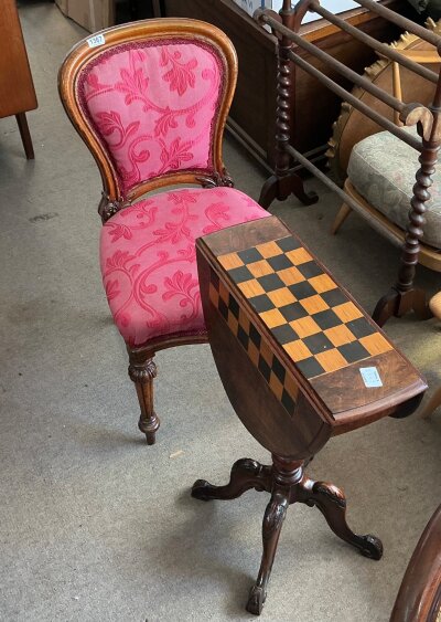 A Victorian walnut games table with a dark coral Victorian chair. The central fixed panel of the games table is beautifully inlaid with a contrasting wood marquetry chessboard layout and the chair features a balloon black walnut frame with a gentle curve and a modern raspberry pink fabric.