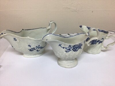 Three early Examples of English porcelain mid 18th century sauce boats cream jugs decorated with underglaze blue and moulded pattern scrolls and acanthus leaves. hairline crack to one and minor chips. (3)
