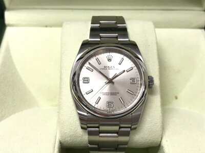 Rolex Oyster Perpetual, featuring a silver dial with luminous stick markers and Arabic numerals at 3, 6, and 9. 2012 model. Serial number G5923**. Box and card with swing tag. Seen running. 36mm case.