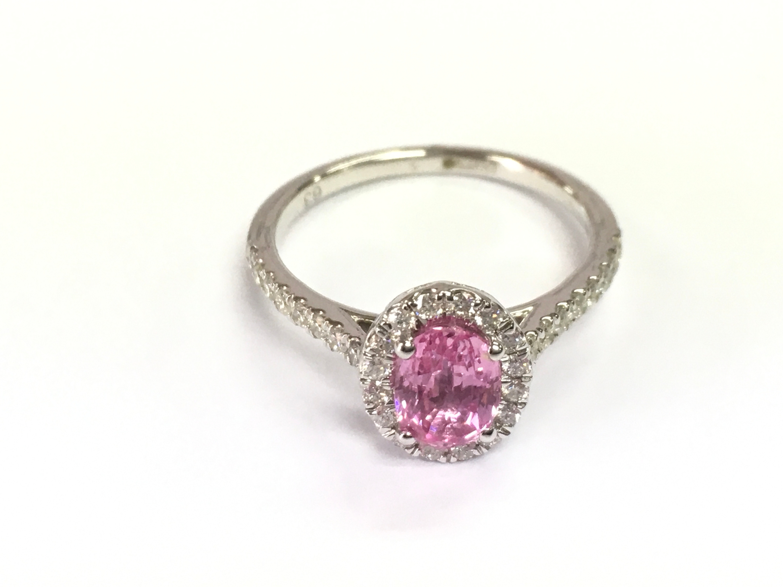 A 9ct white gold oval pink sapphire ring with diamonds set to surround and shoulders. Size O