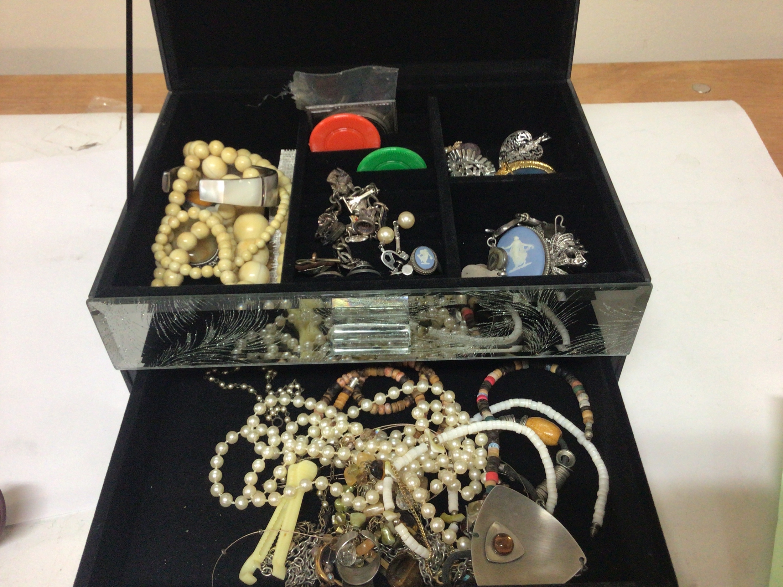 A mirrored glass jewellery box containing costume jewellery some silver jewellery including a charm bracelet.