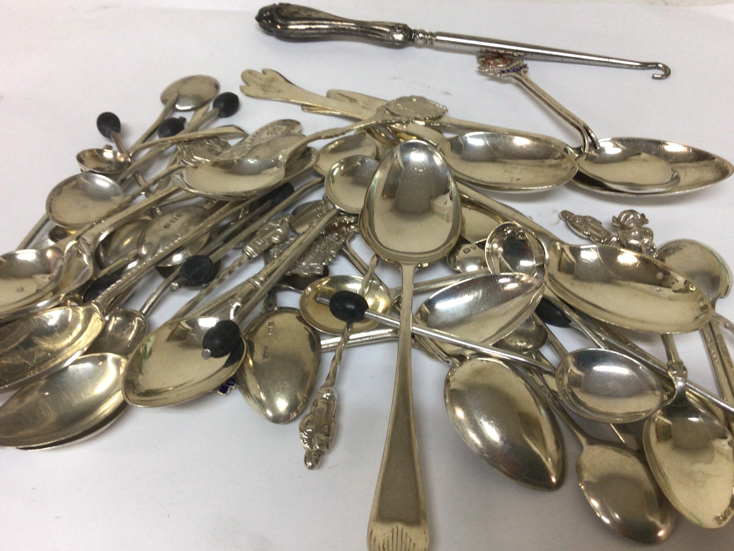 A good selection of mixed silver spoons including tea and coffee spoons enamel decorated spoons weight 480g approximately and a button hook. 