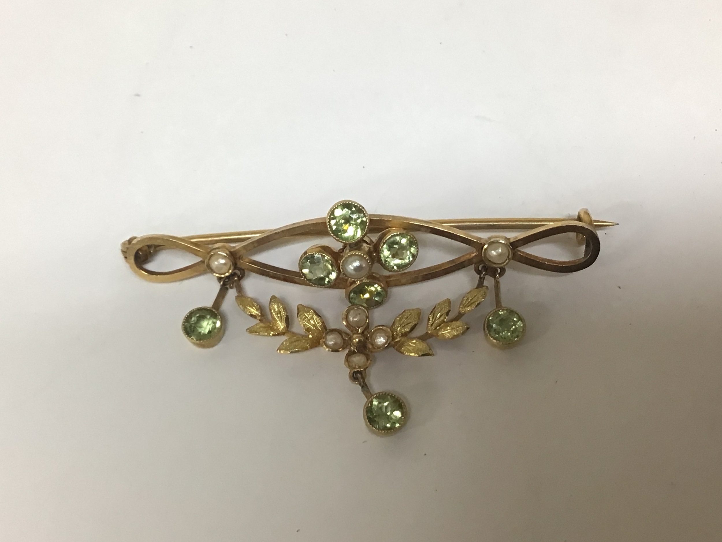    A 9cart gold Vintage brooch set green peridot and seed pearl in the form of a simulated ribbon tie and floral swag. Weight 3.5g 