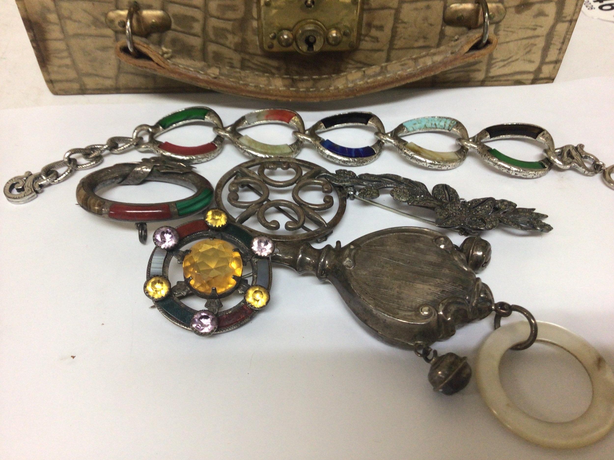 A collection of Scottish silver brooches set with polished stones a child's rattle and other costume jewellery in a Vintage jewellery box. 