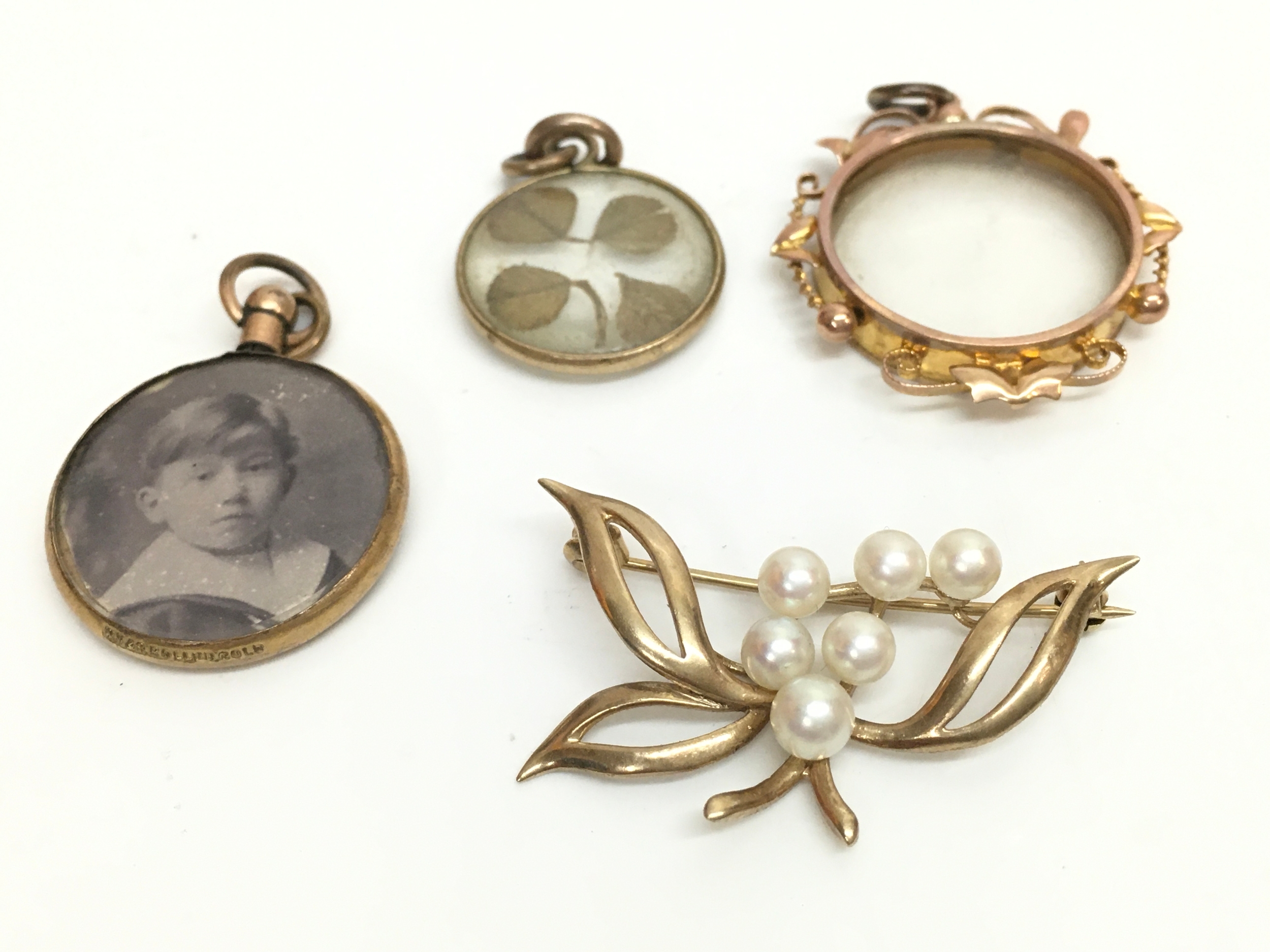Three 9ct gold mounted locket style pendants including a four leaf clover and a 9ct gold pearl brooch. 17g total weight 