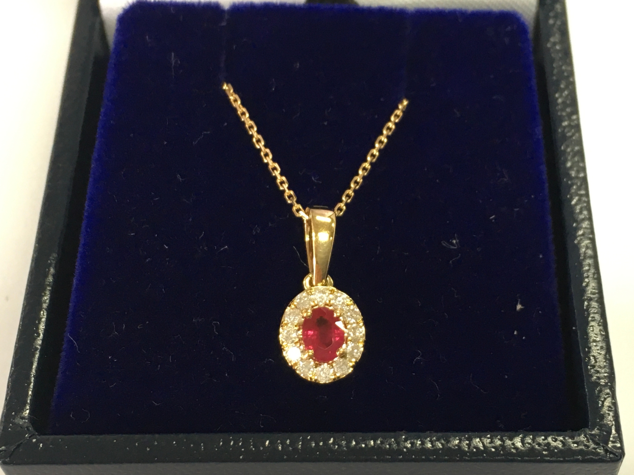 9ct gold oval ruby and diamond cluster pendant on a 9ct gold chain. Ruby 0.32ct and diamonds 0.12ct.