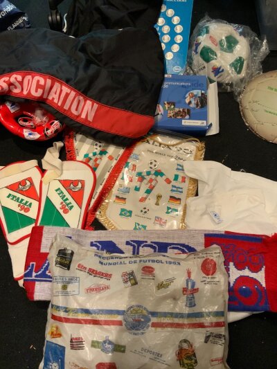World Cup Football Memorabilia Box: 1998 sealed flag, press book with pen, England scarf, ball x 2, t- shirt, 1970 record Back Home, Italy 1990 pennants x 2, shin pads. C/W Football Association bag they used to carry footballs, Portugal Toffs replica shirt. Spotted a 1962 Chile World Cup sponsored bag which we imagine was used to make seating more comfortable.