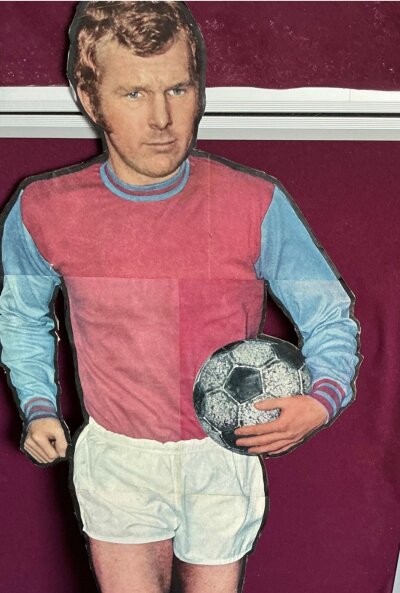 Bobby Moore West Ham Large Cardboard Promotional Display: 42 inch high cardboard cut out of Bobby Moore in West Ham kit with the World Cup believed to be promoting a magazine in the 60s. C/W magazines and pictures of Bobby.