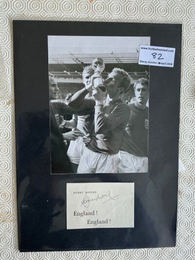 Bobby Moore Signed West Ham + England Football Display: Part of a page taken from his book England England which has been signed in biro without dedication. Stuck down to a large black card which above has a picture of Bobby holding the World Cup. Would fit into standard frame.