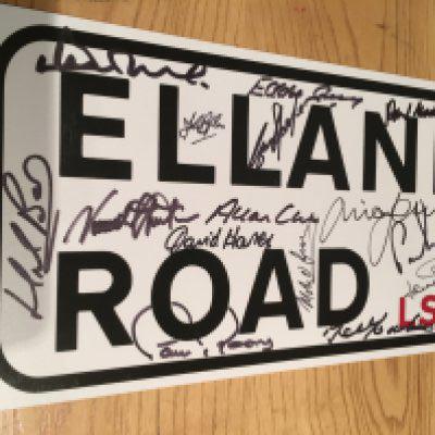 1970s Leeds United Signed Elland Road Sign: Replica 13 inch road sign signed by legends Reaney Gray Hunter Jones Clarke Harvey Charlton OGrady Madeley Bates Lorimer Giles Sprake McKenzie Yorath and Belfitt. Coa from reputable source.