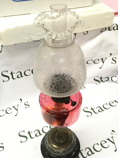 A Victorian cranberry glass oil lamp with a brass column and a porcelain base. Cranberry glass reservoir and a frosted glass shade with etched floral decoration, 64cm tall.