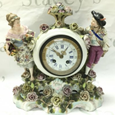 A porcelain clock with raised figures, encrusted with flowers . French movement. Hand missing. Male figures head is damaged. 32cm tall 30cm wide- NO RESERVE