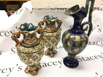 A pair of Victorian continental vases urn shaped with ornate, scrolling handles and elaborate decoration including floral panels on a cream-coloured ground (33cm tall) and an art pottery jug with cobalt blue , hand painted floral decoration and a drip-glaze finish (47cm tall)
