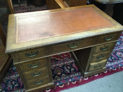 An oak pedestal desk with a tan red leather top, 107cm wide 62cm long 75cm tall.