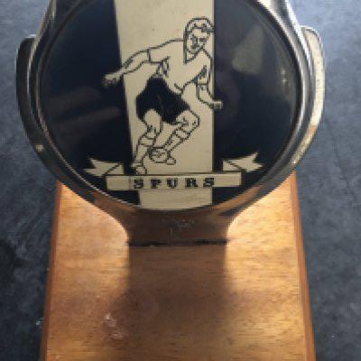 Tottenham Football Memorabilia Box: Original car badge mounted onto a wooden plaque that must be at least 60 years old. C/W away travel pennants in 84/85 to Bohemians and Brugge, FA Cup final rosettes for 81 and 87 and a box of mainly 90s home programmes.