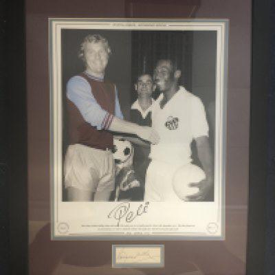 Pele Santos + Bobby Moore West Ham Signed Framed Picture: Large limited edition print of Moore in West Ham kit and Pele in Santos kit in 1970. Pele has signed print number 39/75 and Moores autograph is on white card underneath. Professionally framed with claret and blue board. Not for posting.