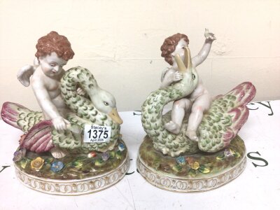 Two conforming porcelain figures with winged cherubs seated on swans the oval bases with raised flowers. Marks to the base.