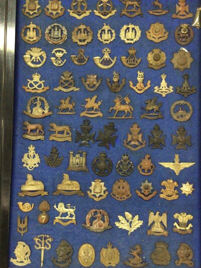 A frame containing a good collection of I world war and other British Military Cap badges many with makers stamp to the reverse