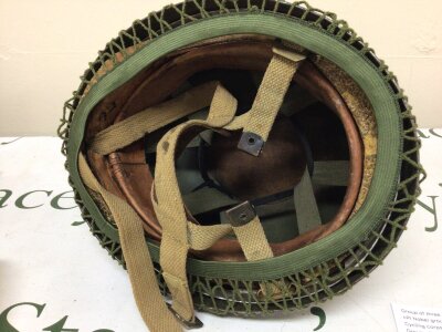 A British Paratroopers Helmet. Possibly II world war or early Cold War issue. The helmet with a later camouflage cover folded edge to the rim and appearing to have original leather early foam and woven straps with a leather chin strap.