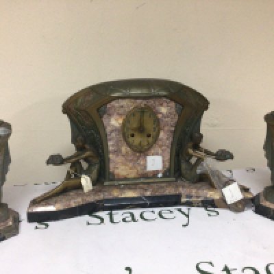 An Art Deco clock garniture the clock with Brocatelle and patterned black marble with coloured metal mounts flanked by two reclining female figures.with matching side ornaments. With key and pendulum. The movement striking on a bell.