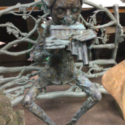 A bronze pixie figure seated playing pipes 120 cm .