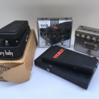 A box of guitar pedals and accessories including a Vox Bulldog distortion, a Blackstar HT-DISTX pedal, a boxed Jim Dunlop Cry Baby wah pedal and others.